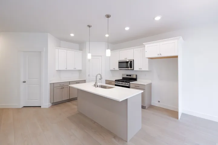 Kitchen featuring a central island with an undermount sink, pendant lighting, white shaker-style upper cabinetry, and stainless steel appliances