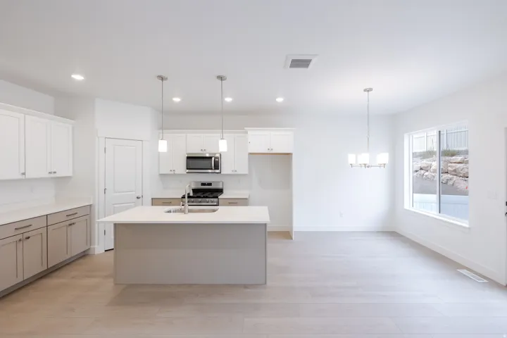 Open-concept kitchen and dining area featuring a kitchen island with sink, stainless steel appliances, two-tone cabinetry, and wood-finish flooring