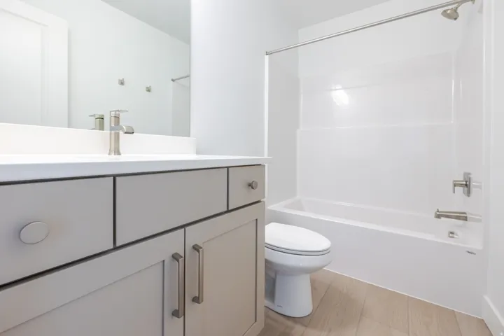 Contemporary bathroom featuring a white vanity top, brushed nickel fixtures, light-toned wood-finish flooring, and a white tub/shower combination
