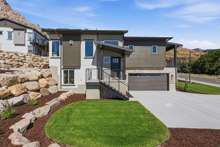 Contemporary two-story residence featuring a dark gray garage door, stacked stone accents, and a covered entryway with black metal railings