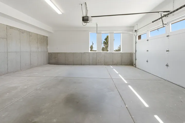 Spacious garage featuring a concrete floor, exposed concrete lower walls, white painted upper walls, and fluorescent ceiling lighting
