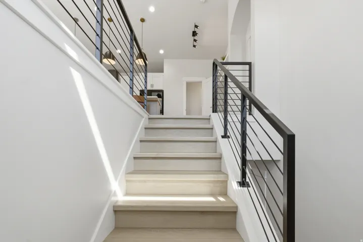 Modern staircase featuring light wood-finish treads and risers, black metal balusters, and white painted walls