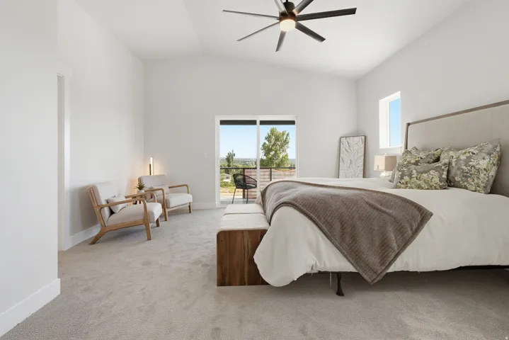Spacious interior featuring a vaulted ceiling with a modern ceiling fan, light-colored carpeting, and a glass sliding door opening to an outdoor balcony