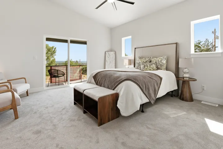 Light-filled bedroom featuring a vaulted ceiling, sliding glass door access to an exterior balcony, and multiple windows