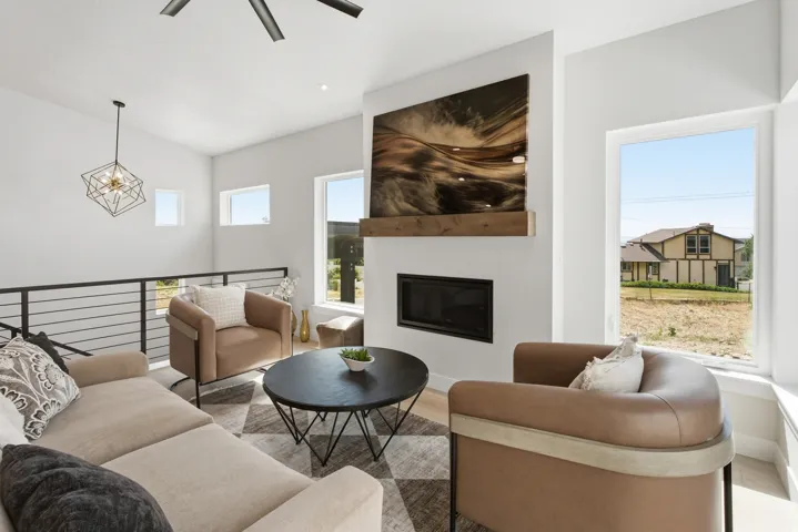 Living area featuring a floor-to-ceiling fireplace with a wood-finish mantel, multiple large windows, and a black metal railing overlooking a lower level