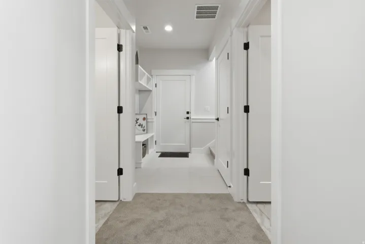 Hallway featuring light gray carpeting, white walls, and multiple white panel doors with matte black hardware