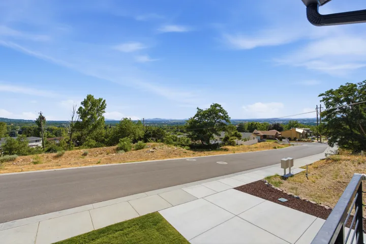 Elevated property with a paved street frontage, concrete sidewalk, and a distant cityscape horizon