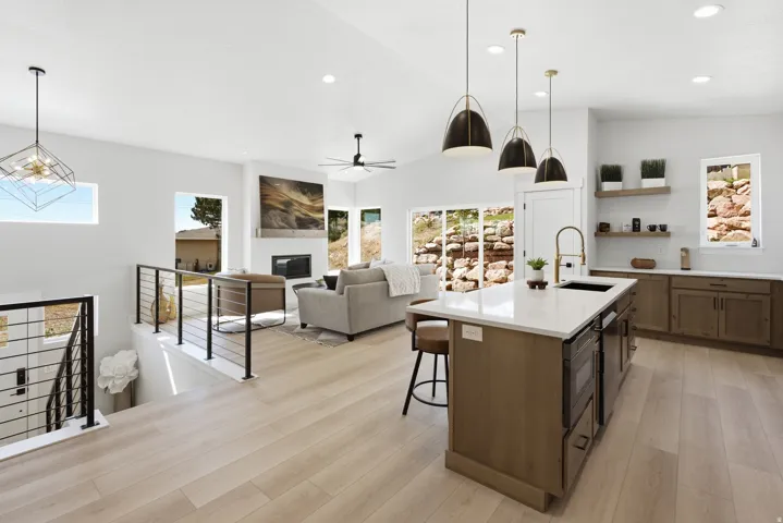 Open-concept living area featuring light wood-finish flooring, a modern kitchen island with an integrated sink and white countertop, and a living room with a fireplace and large windows