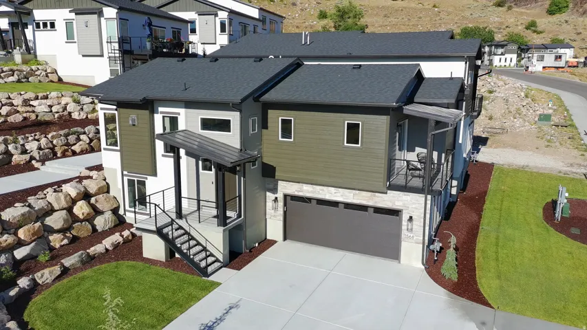Contemporary exterior featuring dark gray roofing, a two-car garage, and a covered front entry with modern metal railings