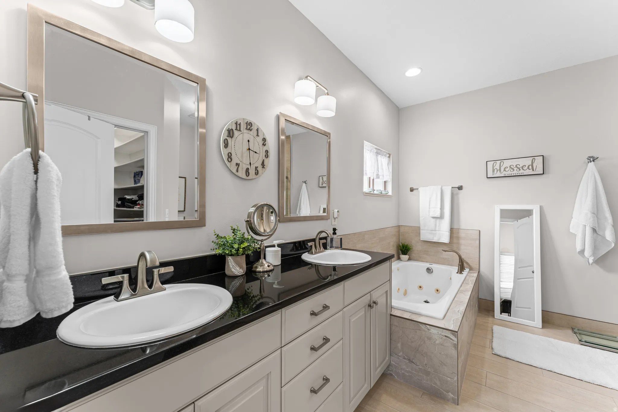 Full bathroom with double vanity, a jetted tub, and light wood-type flooring