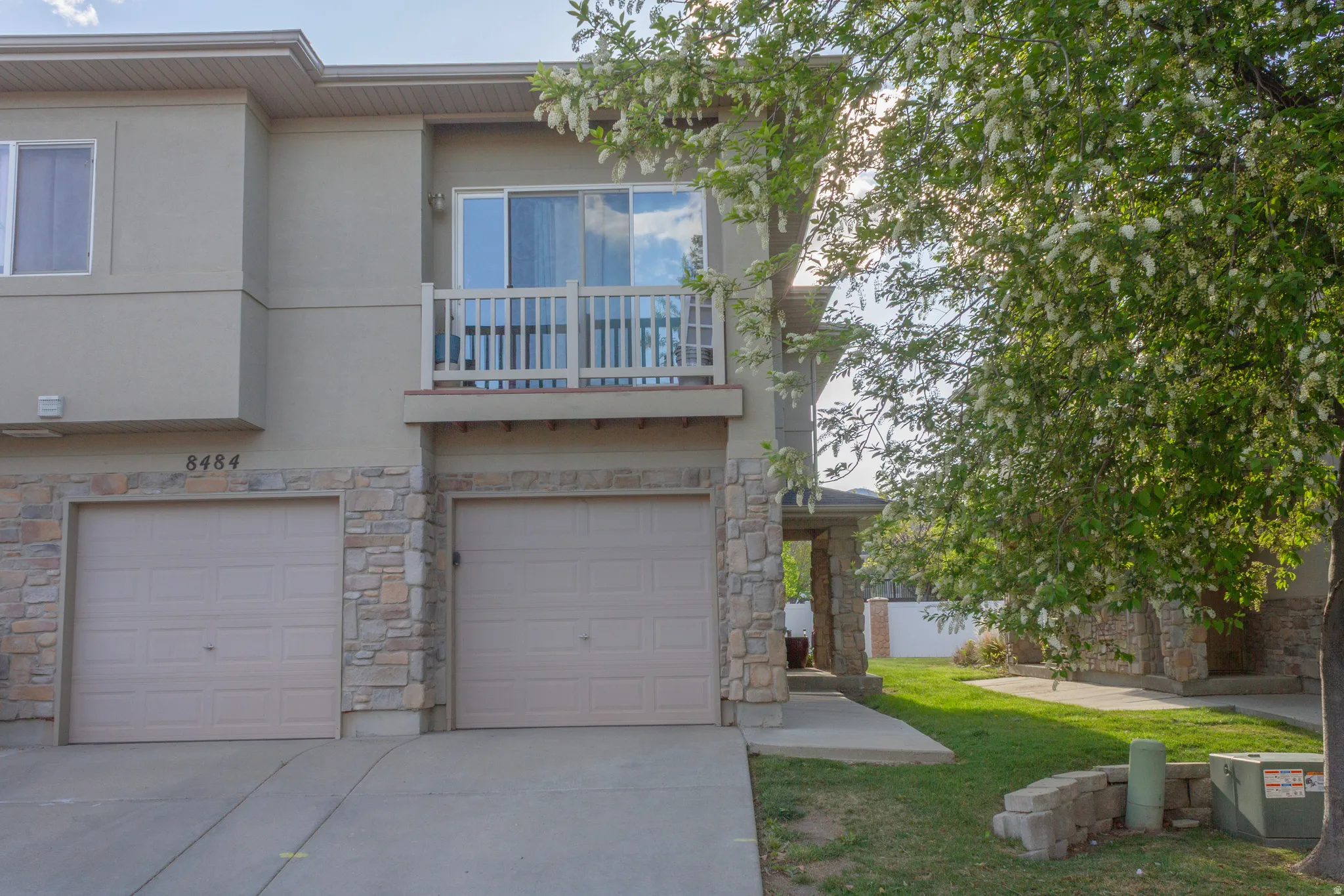 View of front of property featuring a balcony, an attached garage, driveway, stucco siding, and stone siding