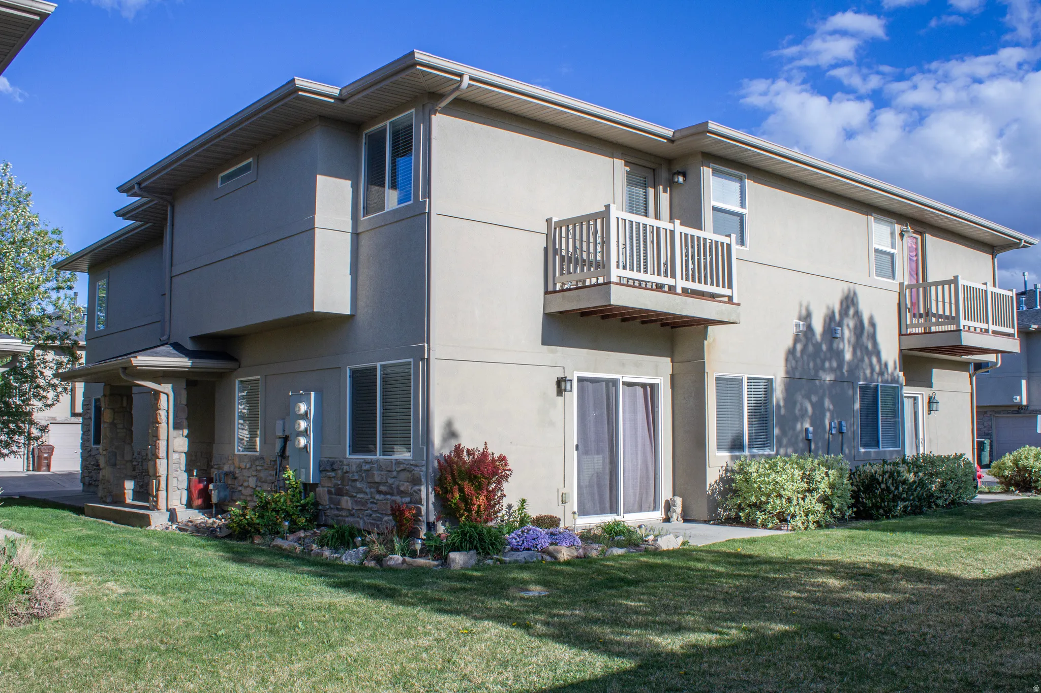 Back of house with a balcony, a yard, stucco siding, and stone siding