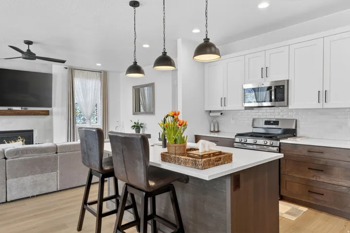 Two tone kitchen with open floor plan, a kitchen bar, stainless steel appliances, ceiling fan, and a fireplace
