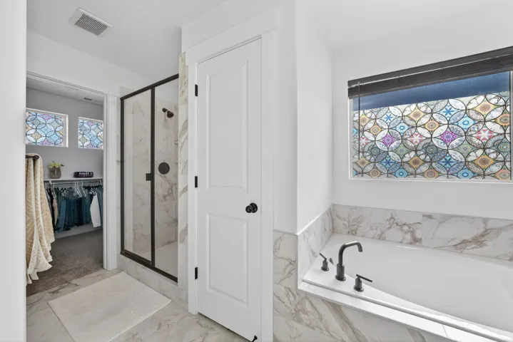 Bathroom with a marble finish shower, a walk in closet, a garden tub, and light marble finish floors