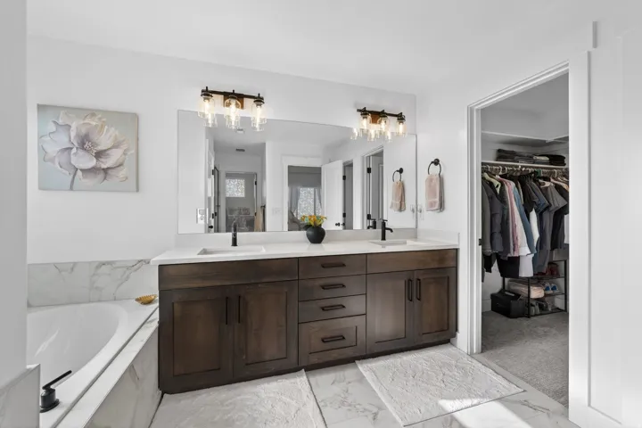 Bathroom with double vanity, a spacious closet, light marble finish flooring, and a bath