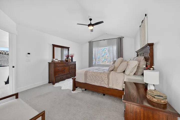 Bedroom with vaulted ceiling, light colored carpet, and ceiling fan