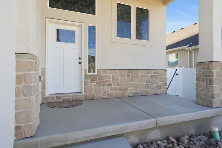 Entrance to property with stone siding, stucco siding, and a patio