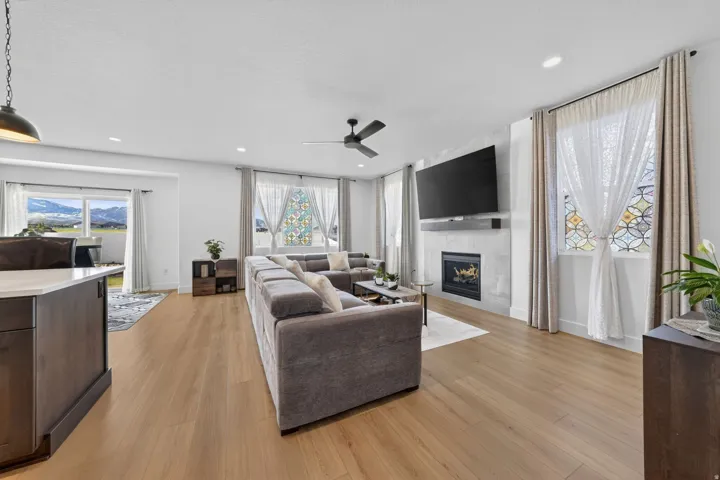 Living area with light wood-style floors, a tiled fireplace, and a ceiling fan