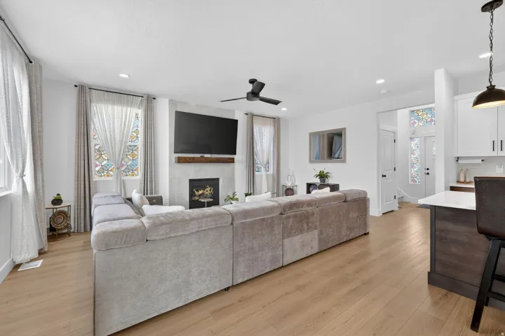 Living room featuring light wood-style flooring, a ceiling fan, a fireplace, and recessed lighting