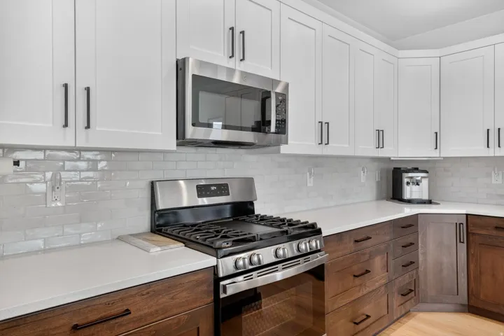 Dual tone kitchen featuring stainless steel appliances, tasteful backsplash, dual tone cabinets, light stone counters, and light wood-style floors