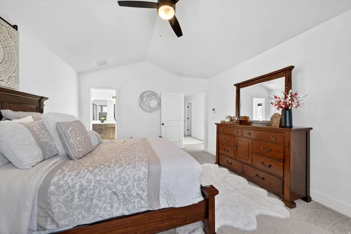 Bedroom with light colored carpet, vaulted ceiling, ensuite bath, and a ceiling fan