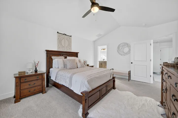 Bedroom featuring light colored carpet, lofted ceiling, ceiling fan, and connected bathroom