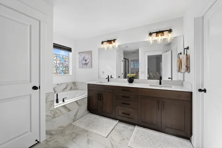 Bathroom with double vanity, a garden tub, and light marble finish floors