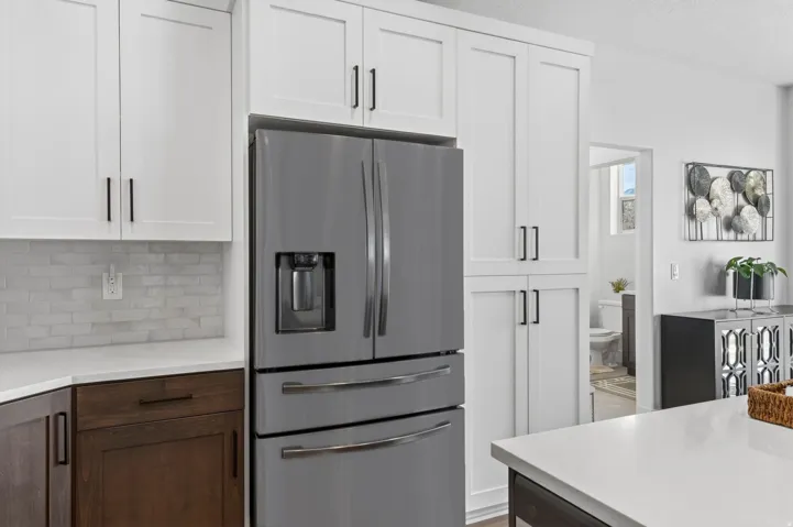 Dual tone kitchen featuring stainless steel refrigerator with ice dispenser, dual tone cabinets, light stone counters, a textured ceiling, and decorative backsplash
