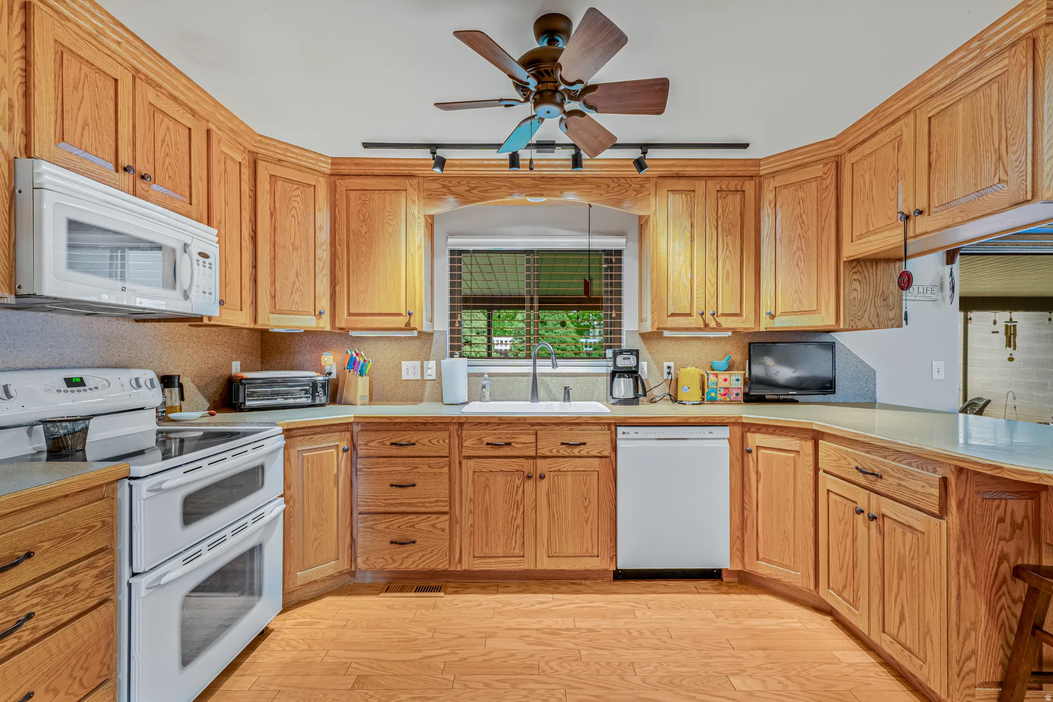 Spacious kitchen with white appliances, light wood finished floors, a ceiling fan, light countertops, and rail lighting