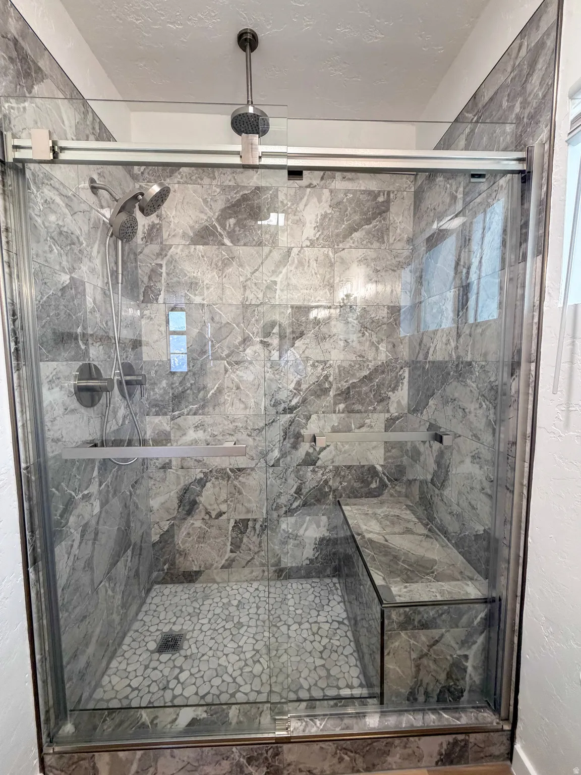 Bathroom featuring a textured ceiling, a textured wall, and a marble finish shower