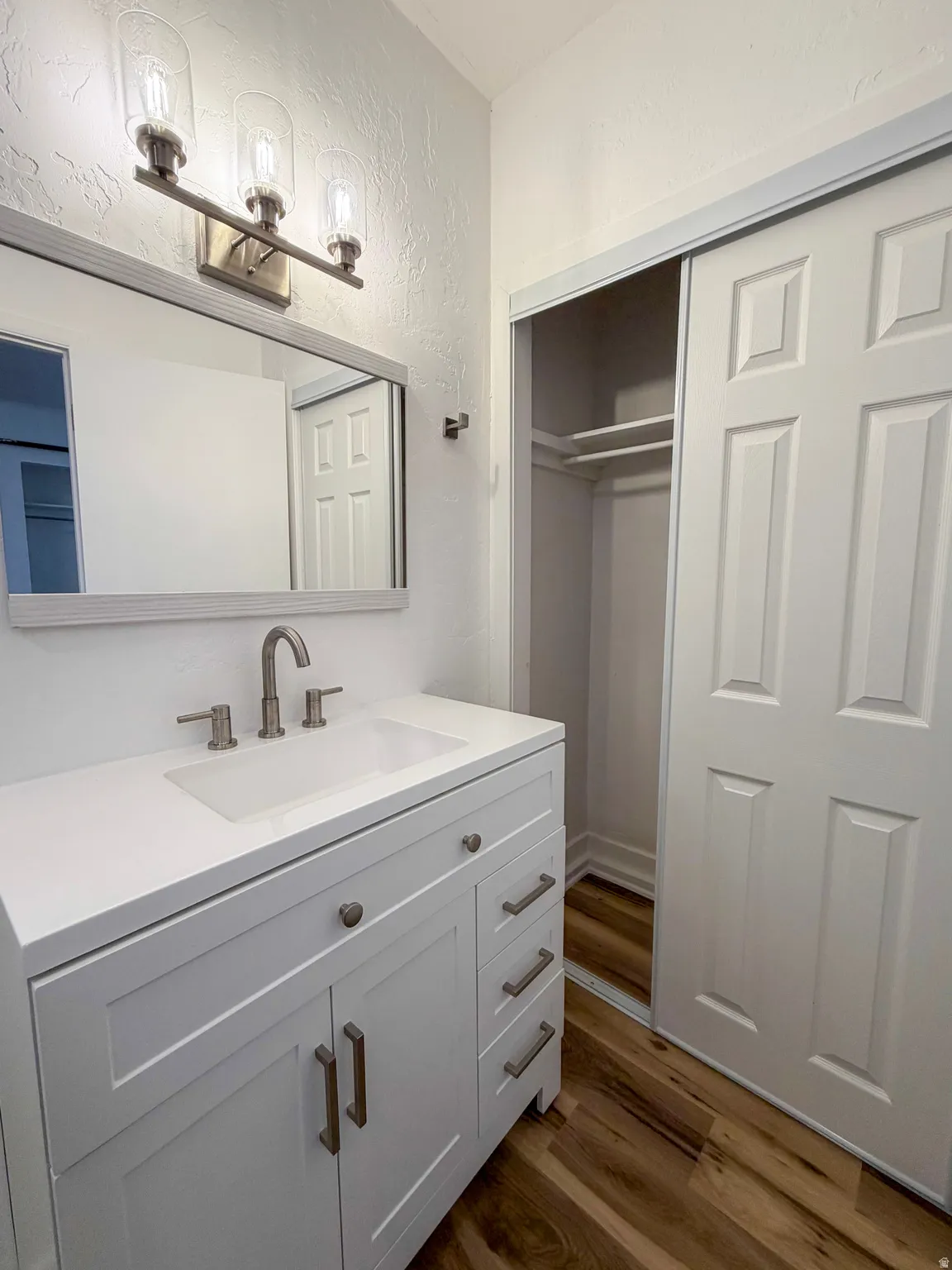 Bathroom with vanity, a textured wall, and dark wood-style flooring
