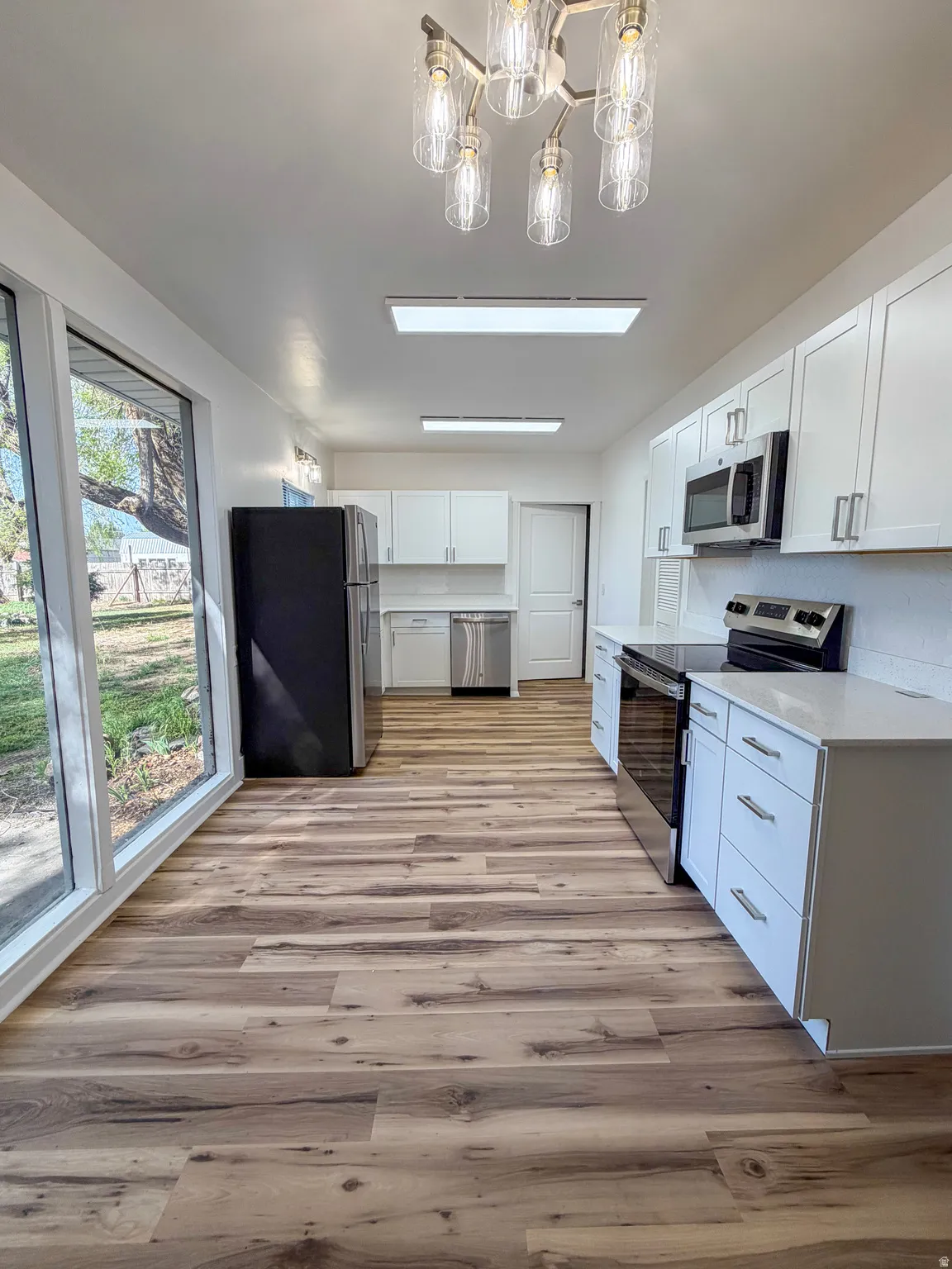 Kitchen with stainless steel appliances, white cabinetry, light wood finished floors, and suspended lighting