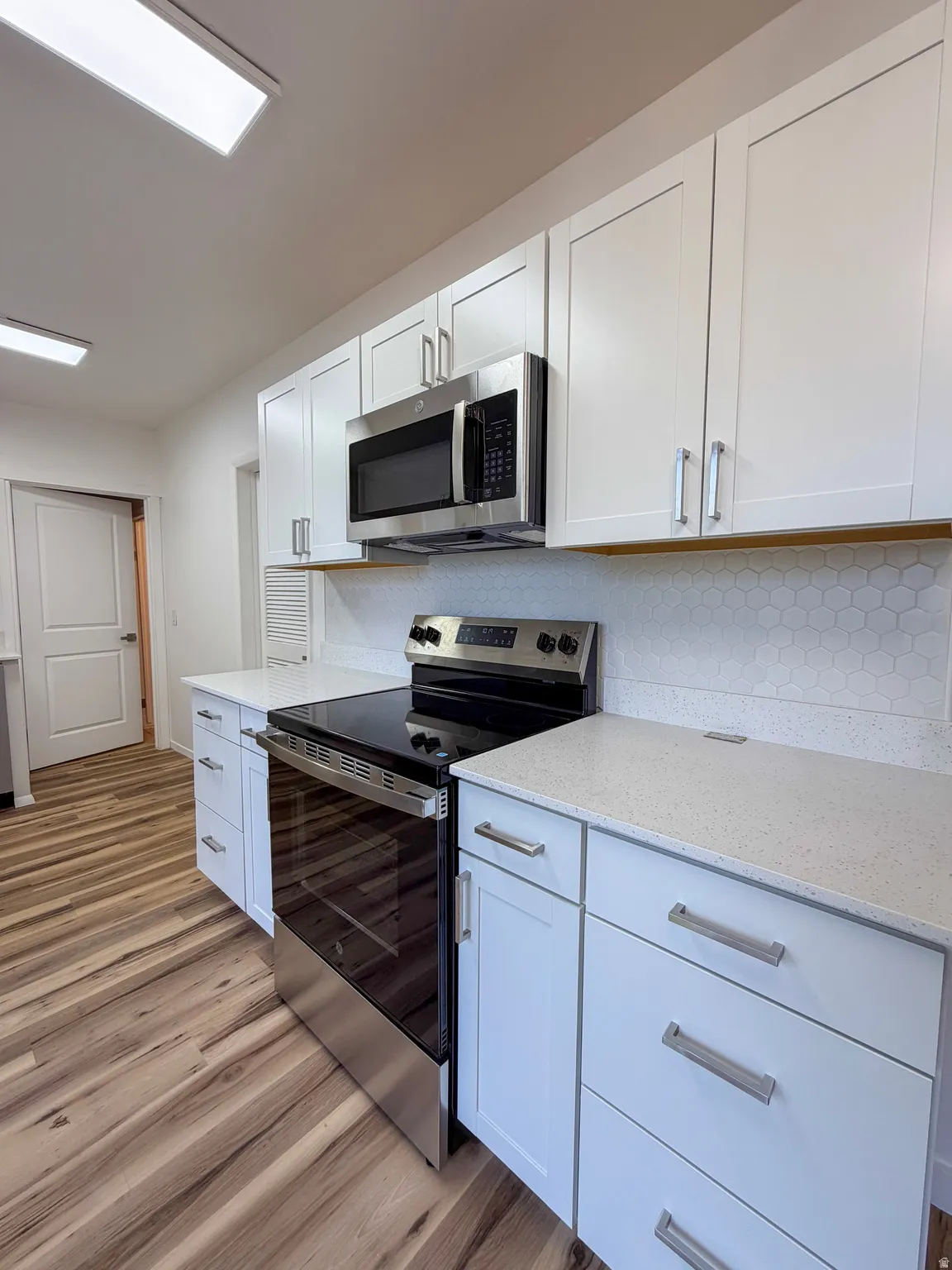 Kitchen with stainless steel appliances, white cabinets, light stone countertops, and light wood-type flooring