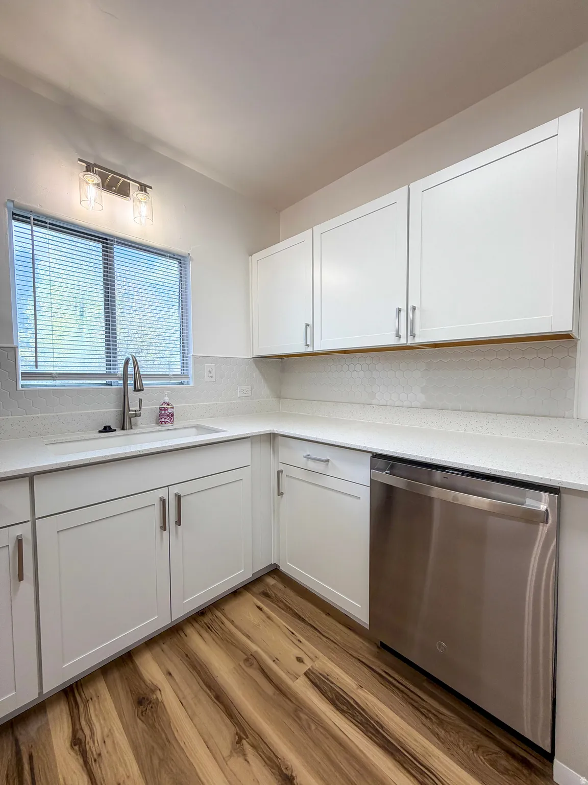Kitchen featuring white cabinetry, stainless steel dishwasher, light wood-style flooring, and light stone countertops