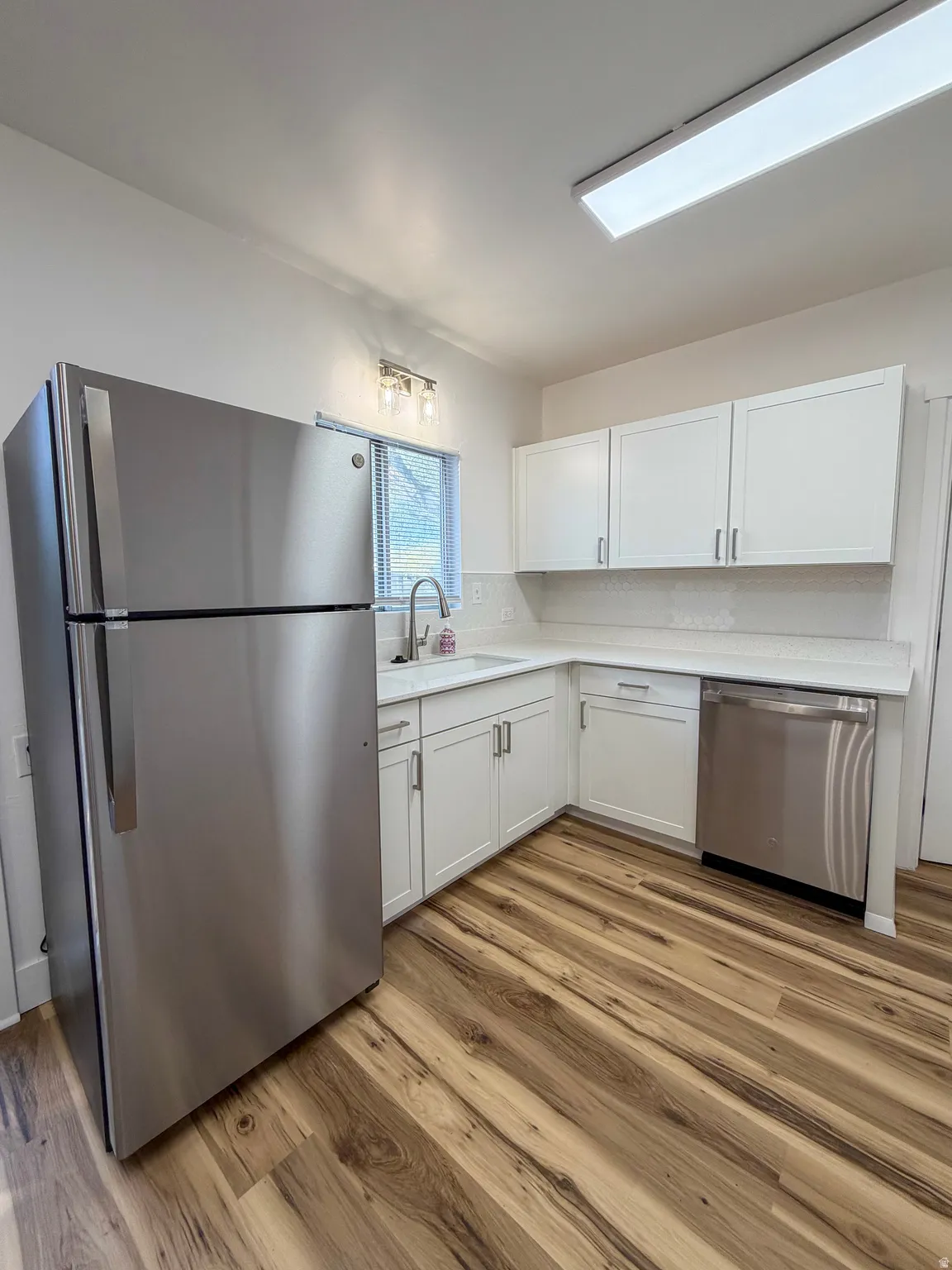 Kitchen with stainless steel appliances, light countertops, white cabinetry, and light wood finished floors