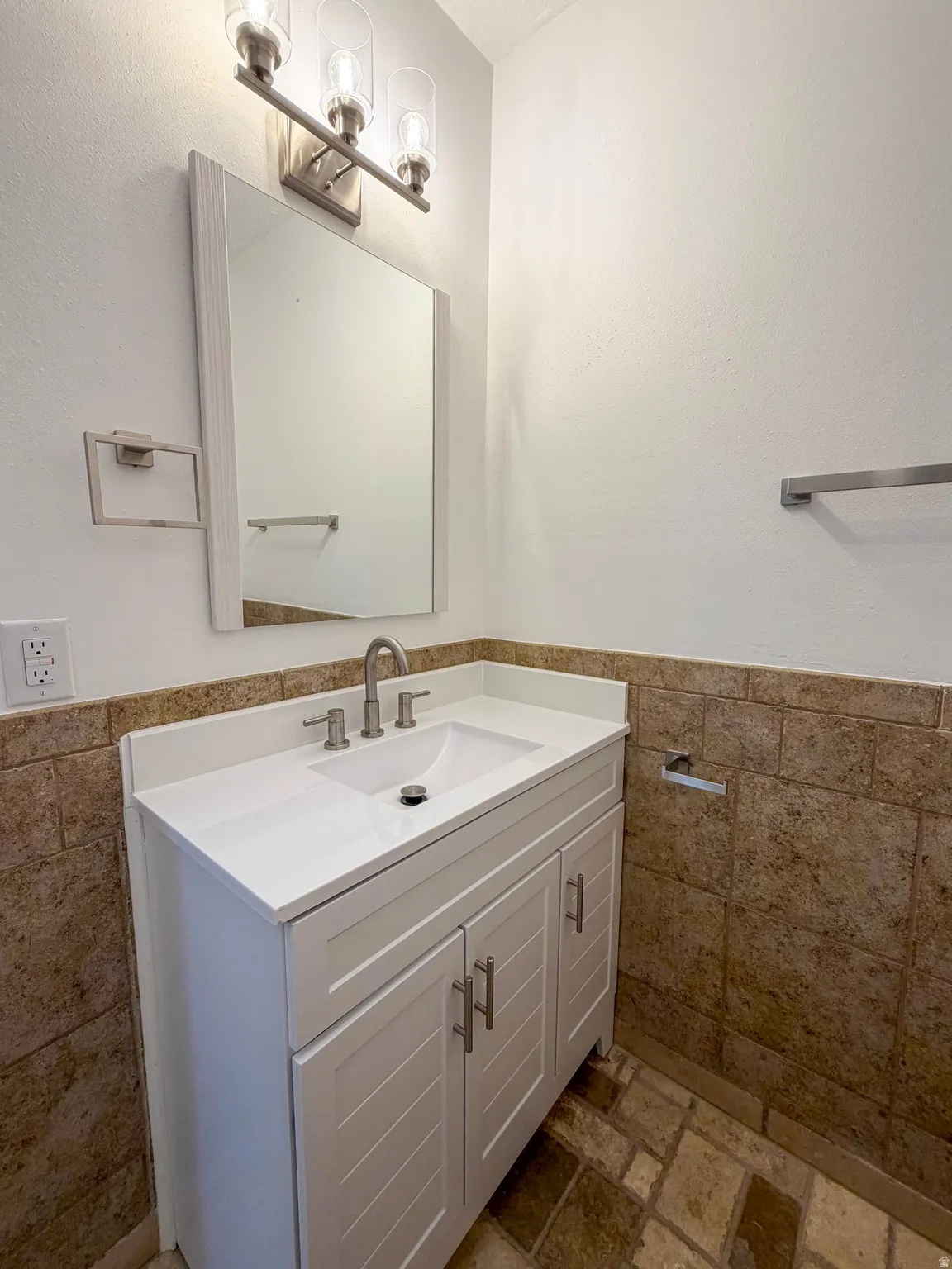 Bathroom featuring tile walls, vanity, a wainscoted wall, and stone tile flooring