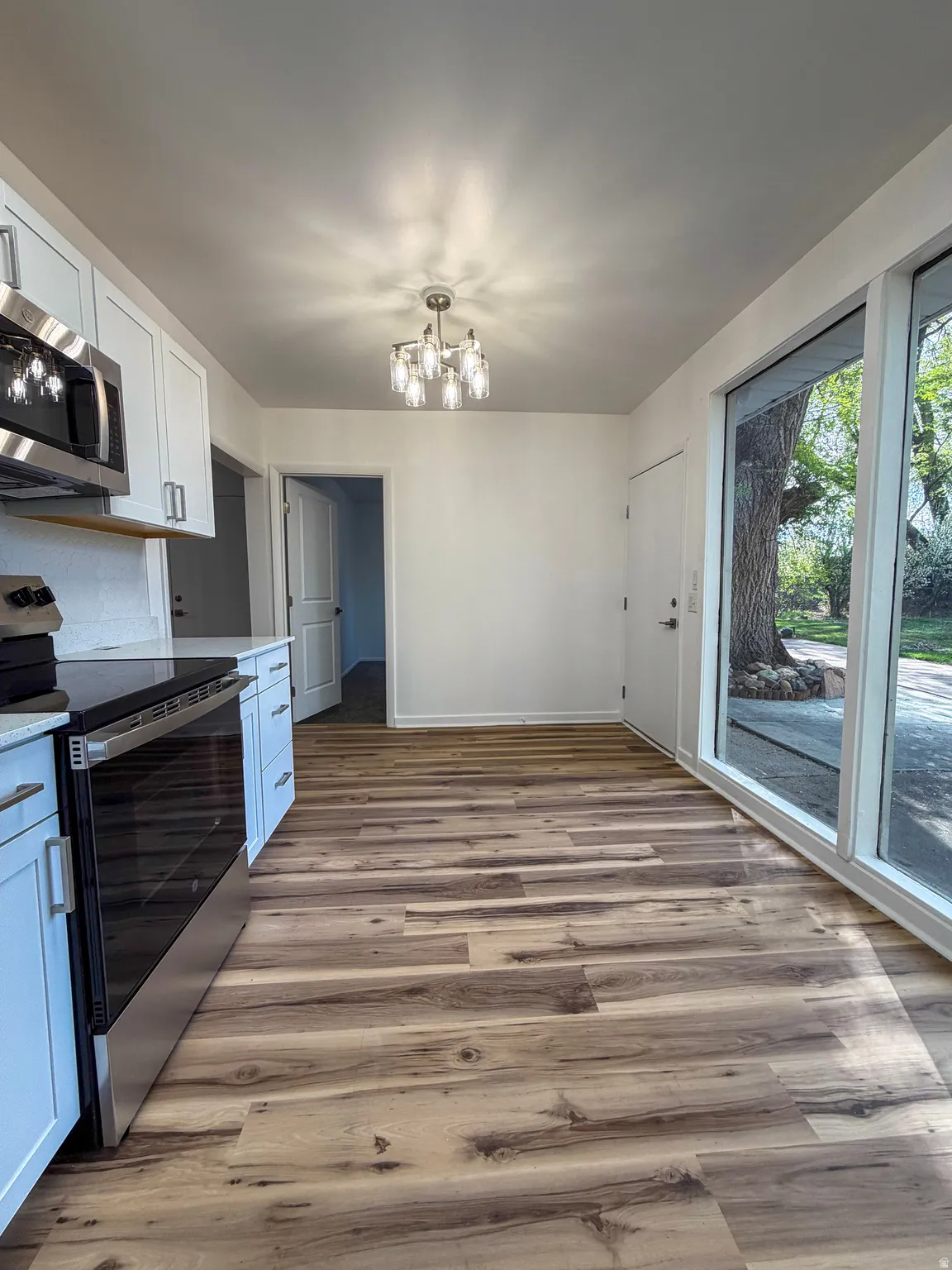Kitchen featuring stainless steel appliances, white cabinets, light wood finished floors, a chandelier, and light stone countertops