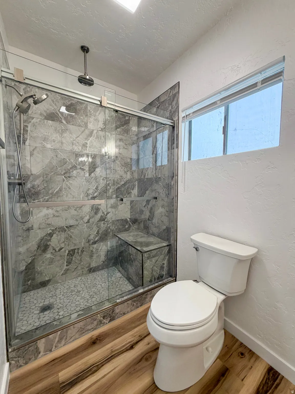 Bathroom with a textured wall, a textured ceiling, a marble finish shower, and wood finished floors