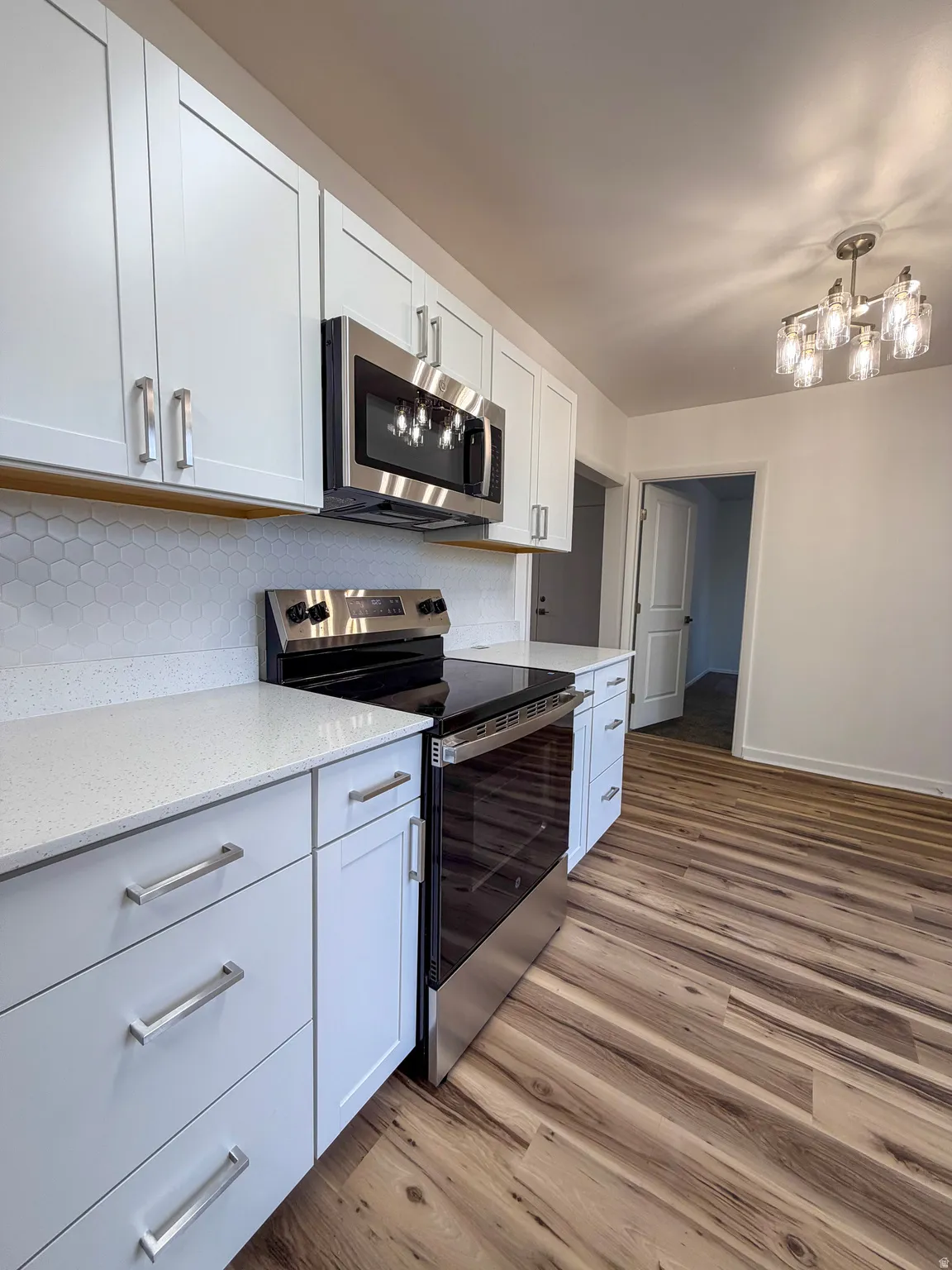 Kitchen with stainless steel appliances, white cabinetry, light wood-style flooring, and light stone countertops