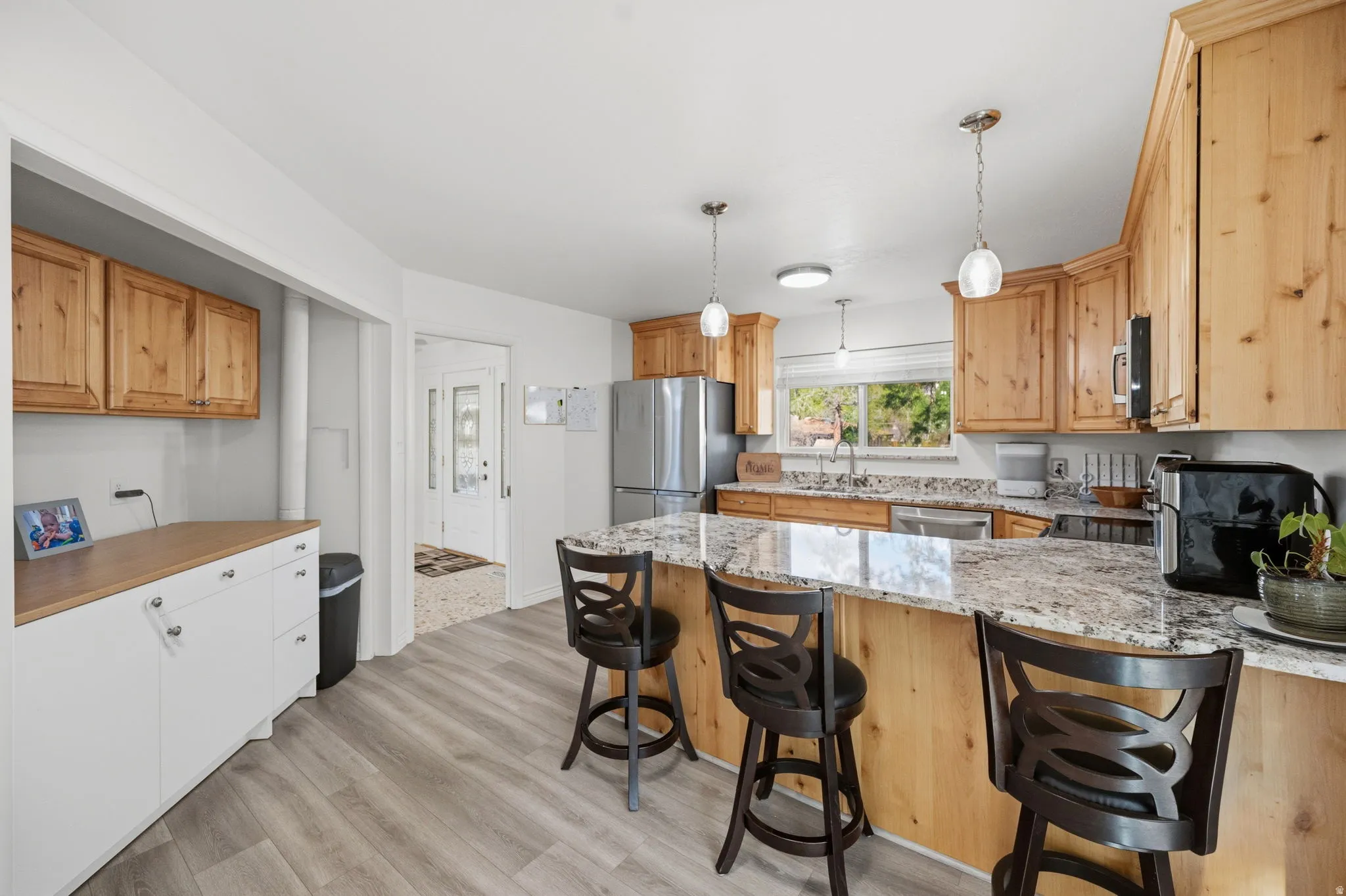 Kitchen featuring light wood-style floors, stainless steel appliances, hanging light fixtures, light stone counters, and a breakfast bar