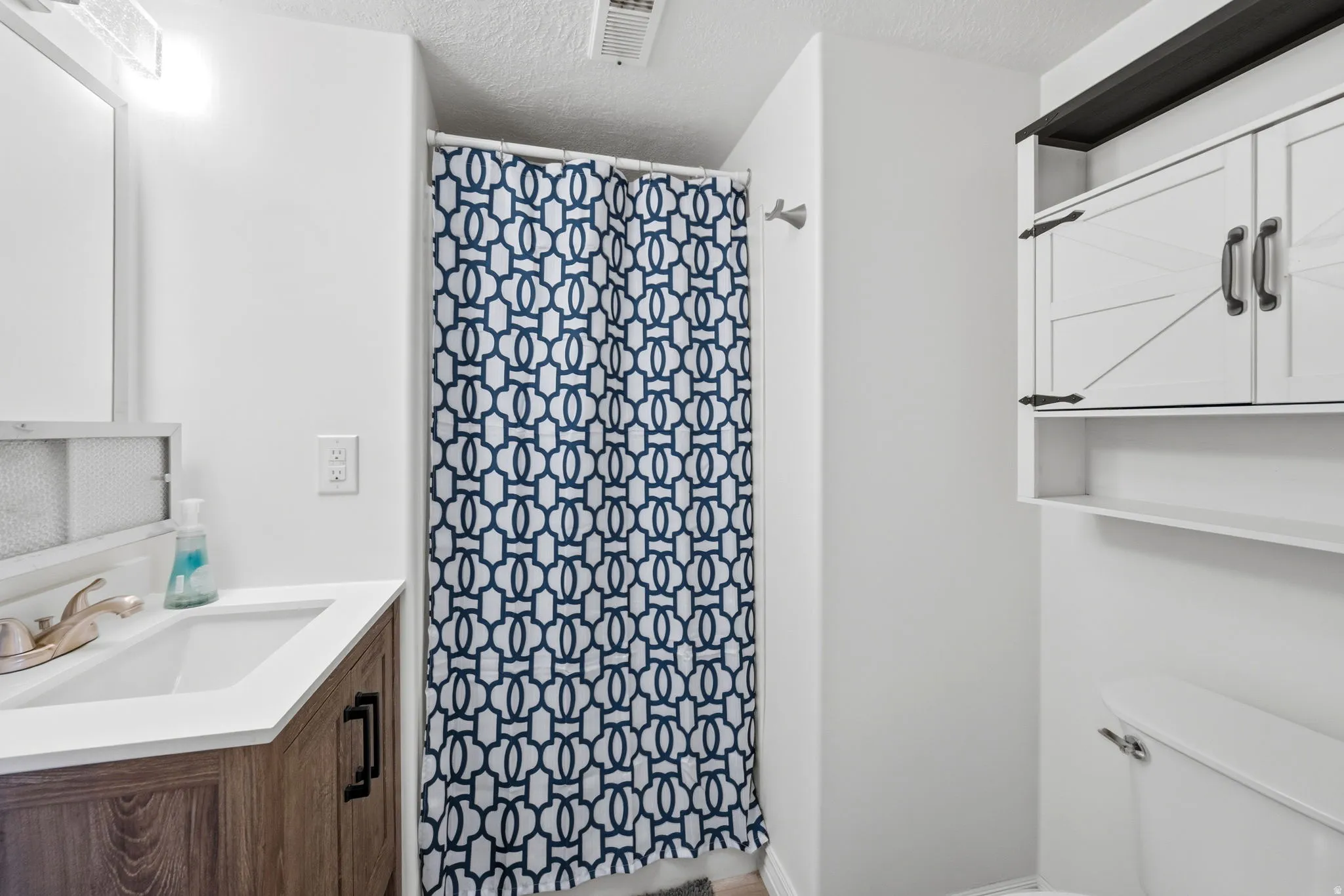 Full bath featuring a shower with shower curtain, a textured ceiling, and vanity