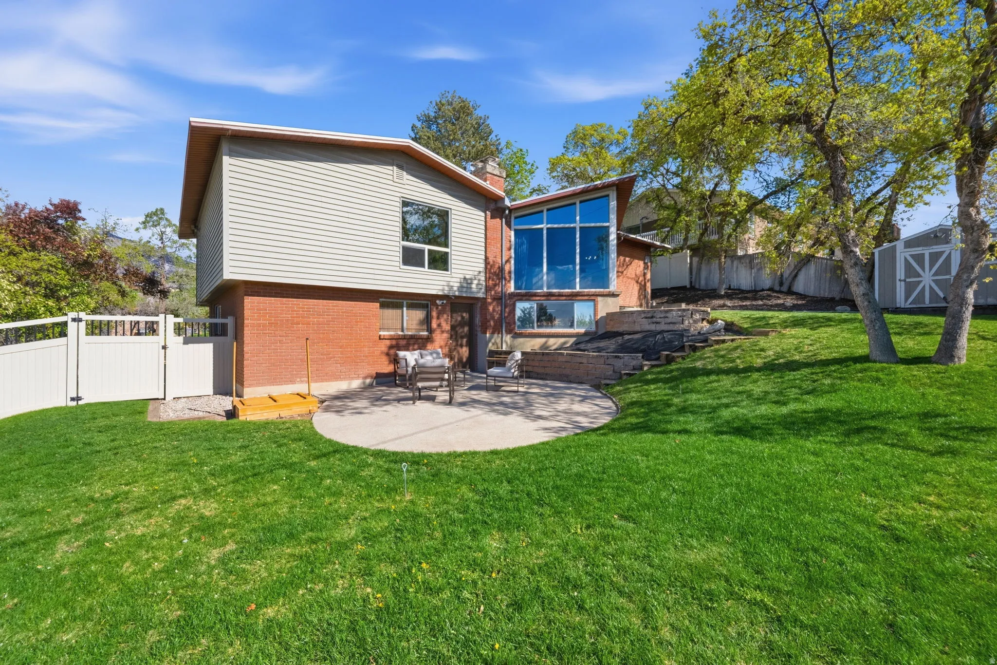 Back of property featuring a patio, a chimney, a fenced backyard, brick siding, and a storage unit