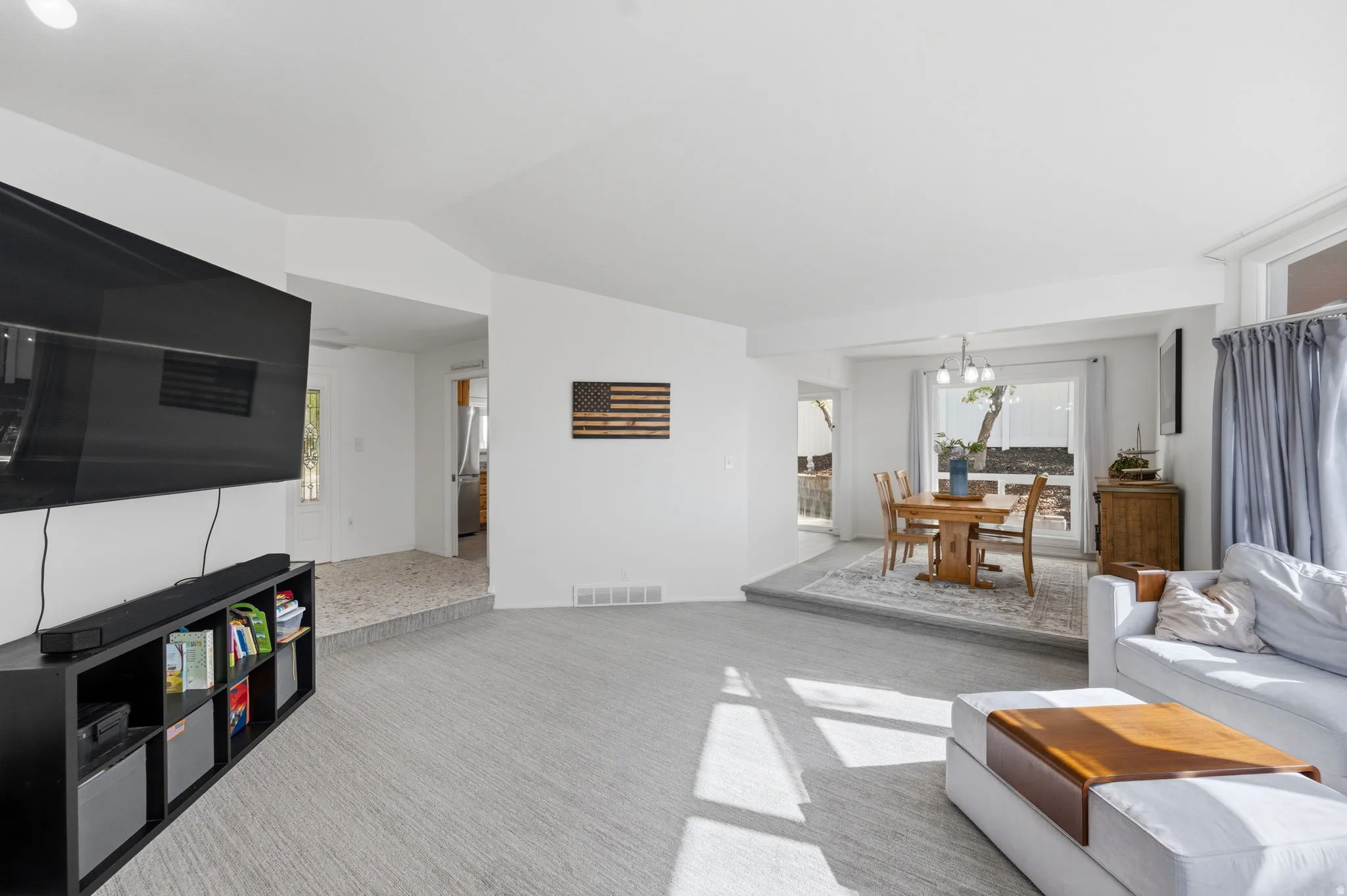 Living area featuring plenty of natural light, vaulted ceiling, light colored carpet, and a chandelier