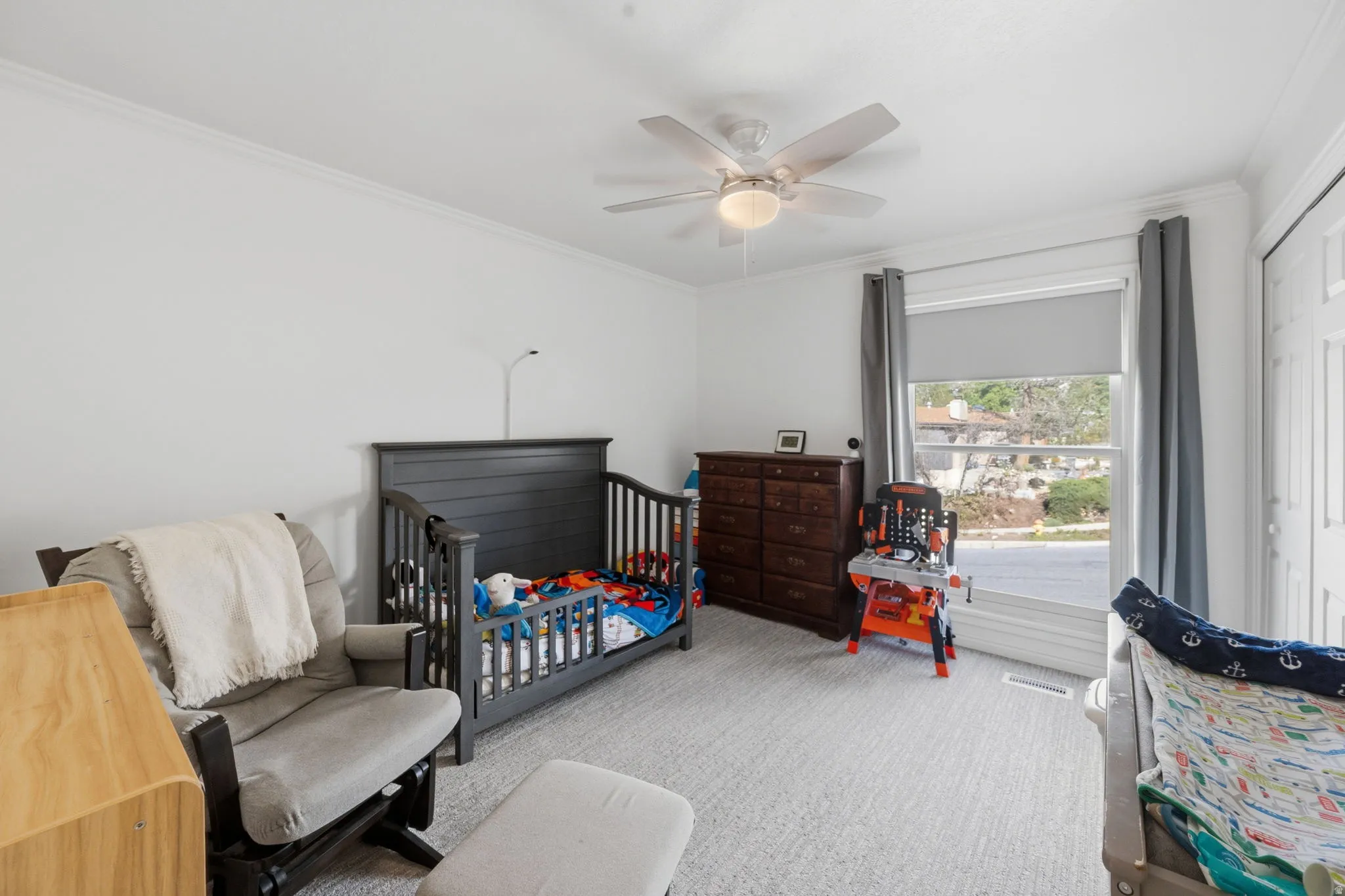 Bedroom featuring light carpet, crown molding, a ceiling fan, and a nursery area