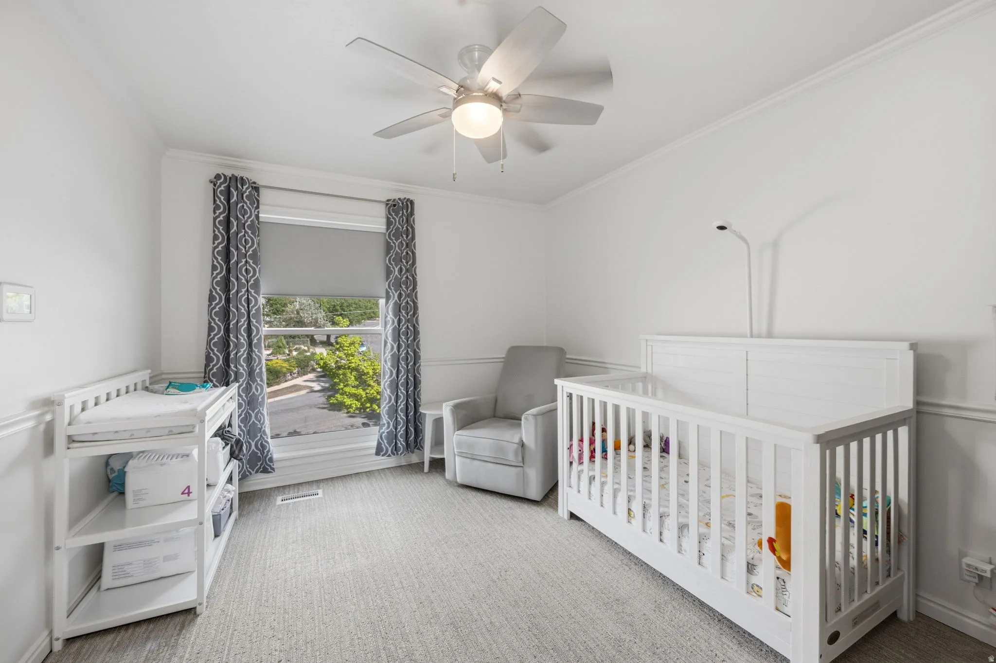 Bedroom featuring light colored carpet, a crib, ceiling fan, and crown molding