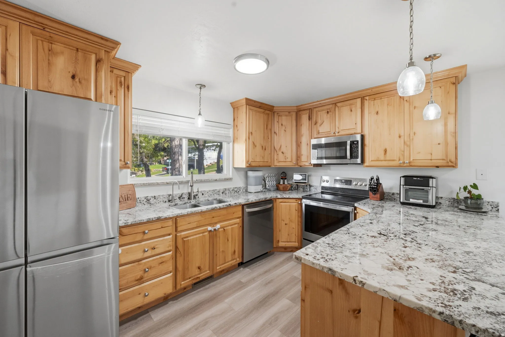 Kitchen featuring stainless steel appliances, hanging light fixtures, and light stone countertops