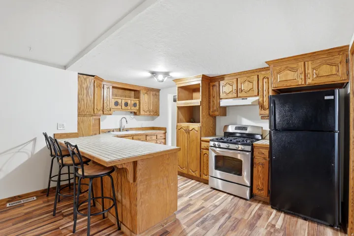 Kitchen with freestanding refrigerator, a kitchen bar, open shelves, stainless steel gas range oven, and a textured ceiling