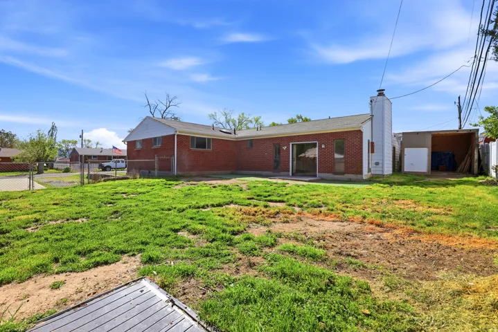 Rear view of house featuring a fenced backyard, brick siding, a patio area, a gate, and a chimney