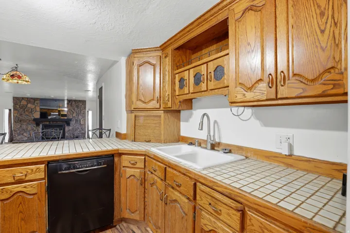 Kitchen featuring black dishwasher, a fireplace, tile countertops, and a textured ceiling