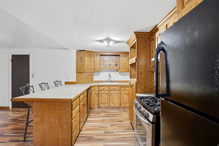 Kitchen featuring a peninsula, freestanding refrigerator, a kitchen breakfast bar, light wood finished floors, and stainless steel range with gas cooktop
